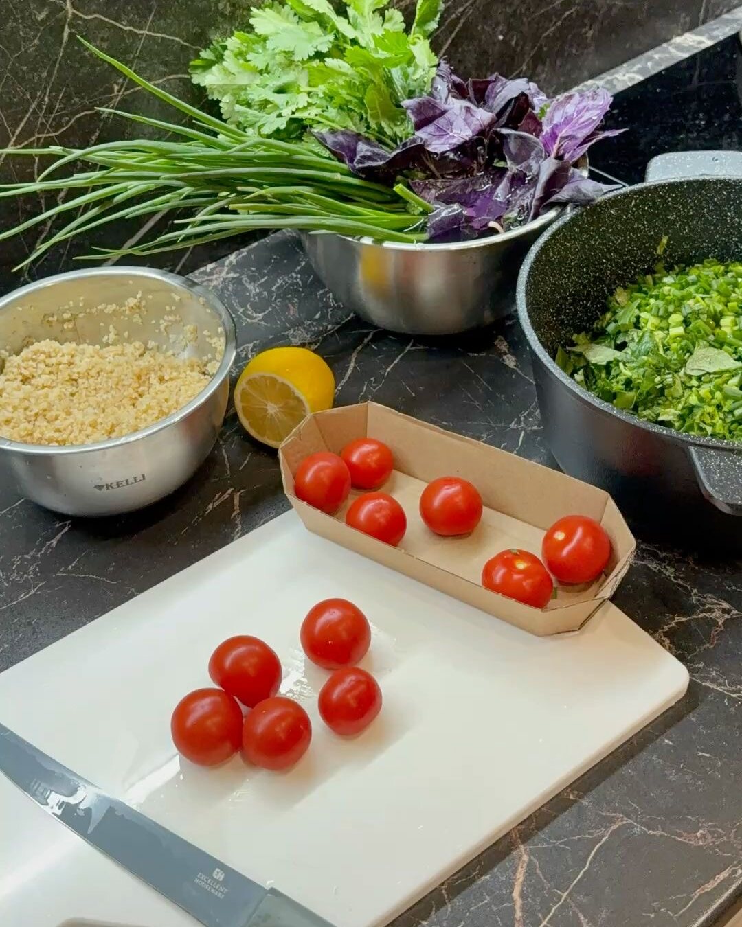 Fresh herbs, cherry tomatoes, lemon and bulgur laid out on a kitchen counter