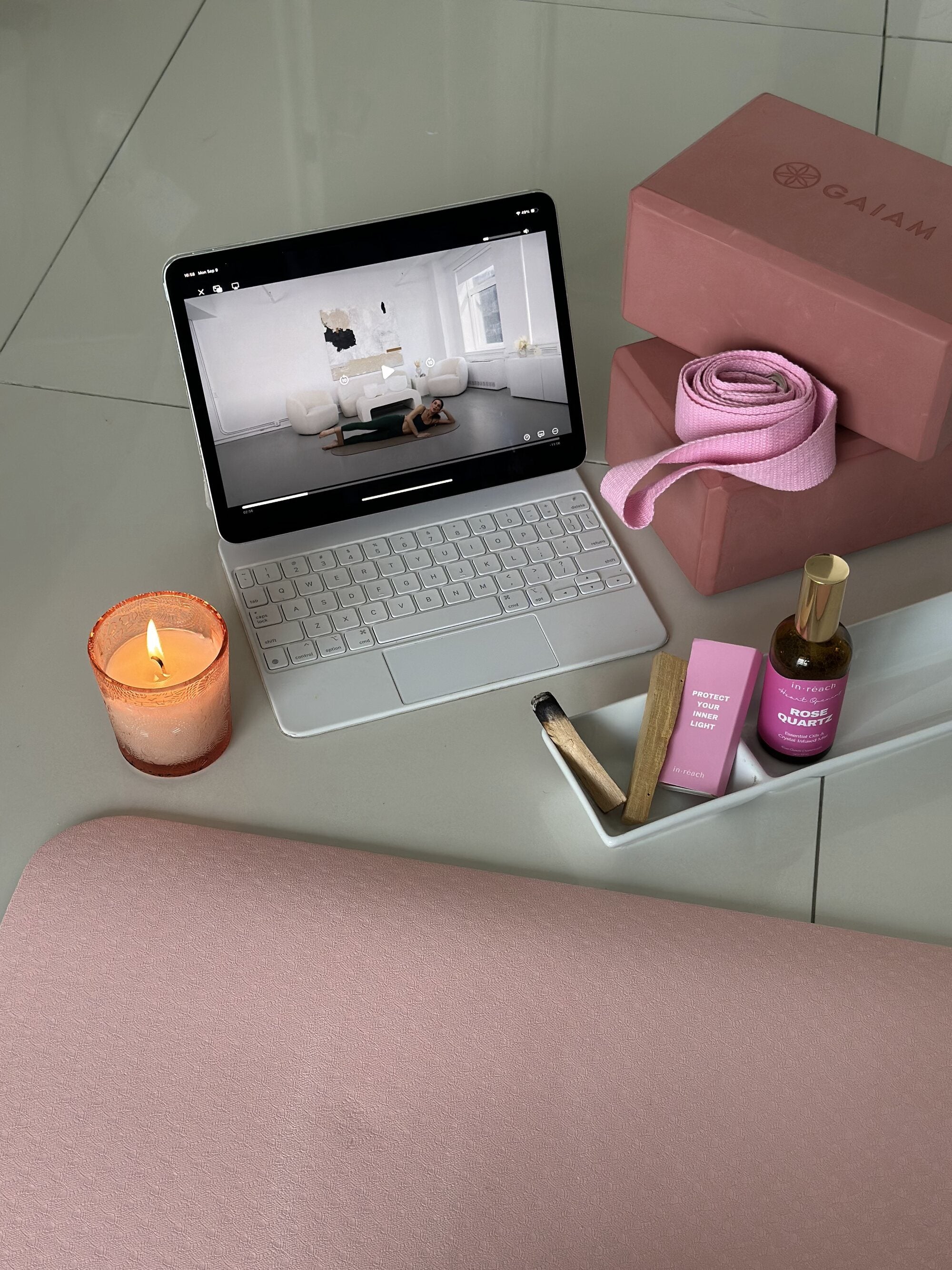 An in·reach Pilates class streaming on a tablet beside a pink mat, yoga blocks, strap and a lit candle